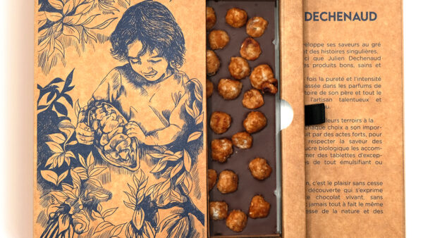 Tablette de chocolat noir et noisettes du Piémont caramélisées du chef Julien Dechenaud chocolatier à Paris et Vincennes. La tablette est dans son étui illustré de fève de cacao