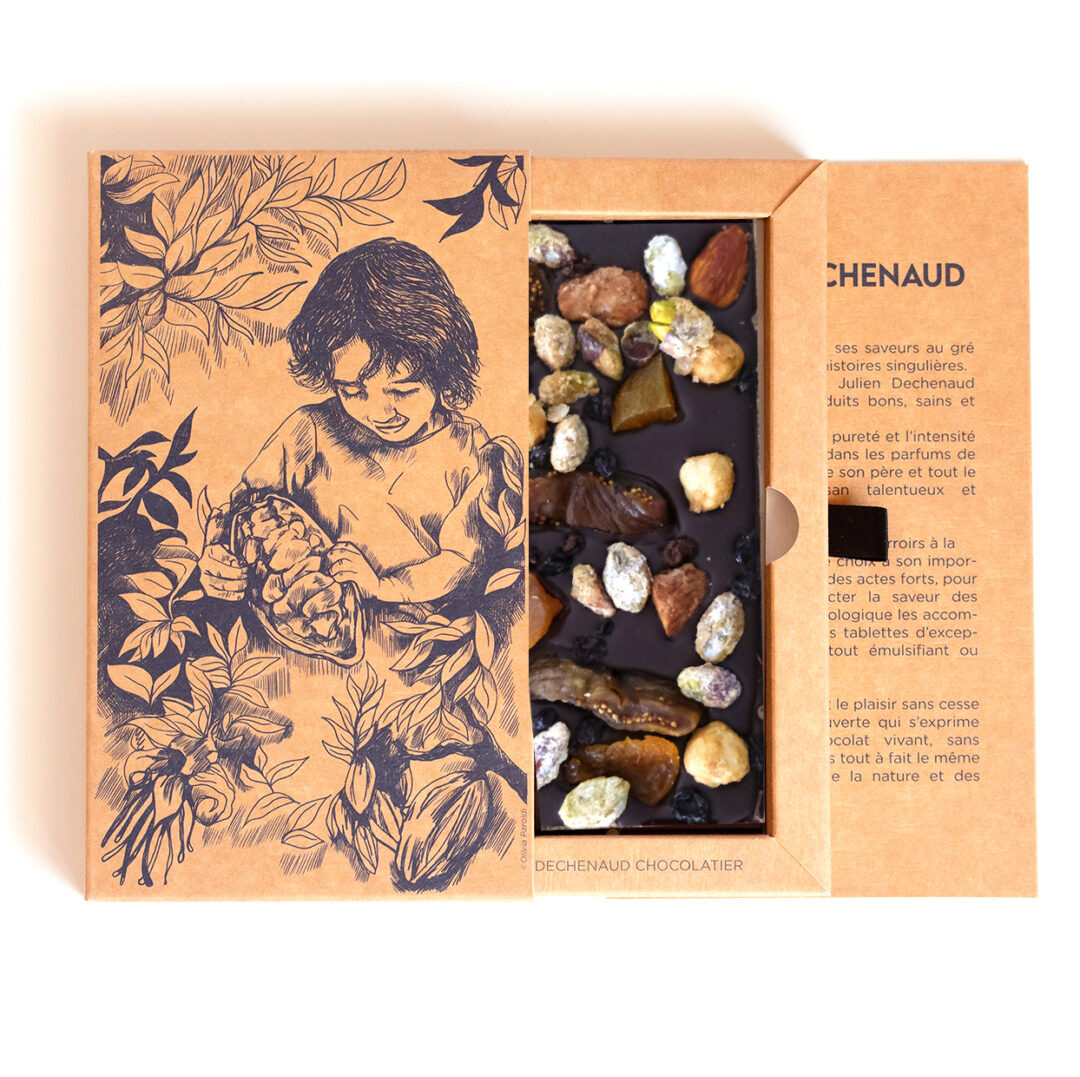 Tablette de chocolat noir avec des amandes et des noisettes caramélisées, des pistaches, des figues et des abricots secs, des raisons de Corinthe. Chocolat du chef Julien Dechenaud chocolatier à Paris et Vincennes. La tablette est dans son étui illustré de fève de cacao