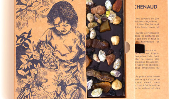 Tablette de chocolat noir avec des amandes et des noisettes caramélisées, des pistaches, des figues et des abricots secs, des raisons de Corinthe. Chocolat du chef Julien Dechenaud chocolatier à Paris et Vincennes. La tablette est dans son étui illustré de fève de cacao